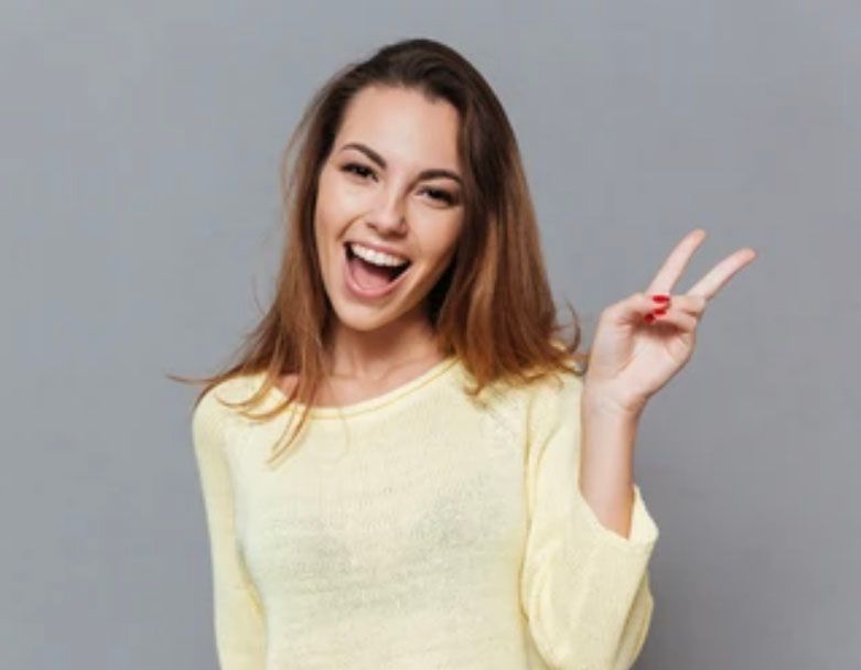 A woman in a yellow sweater is making a peace sign with her fingers.