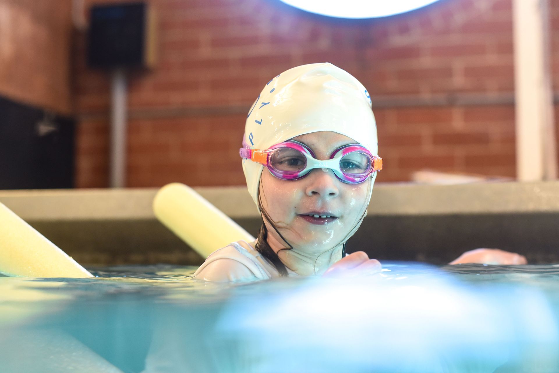 A young girl wearing a swim cap and goggles is swimming in a pool.