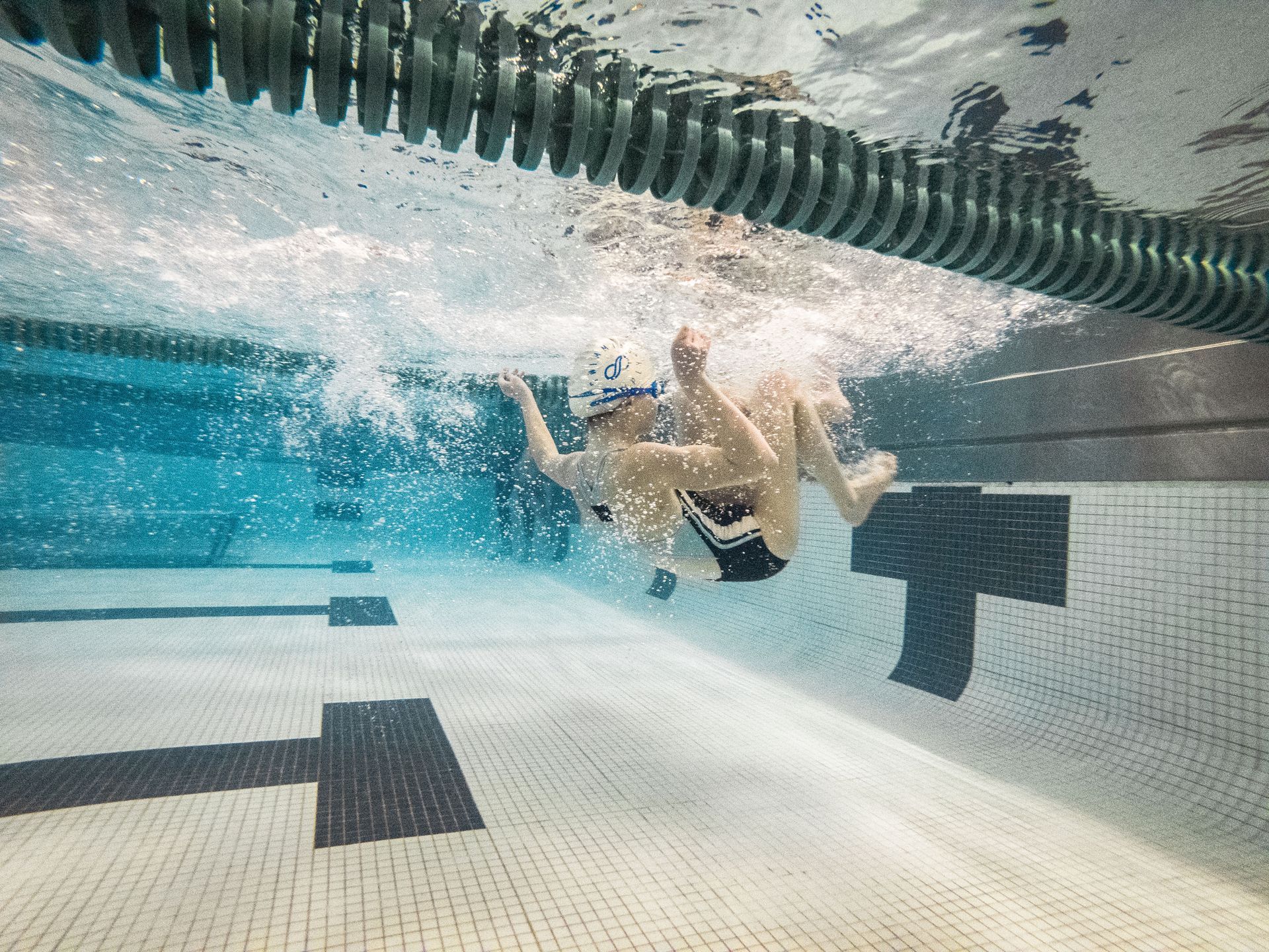 A couple of people are swimming underwater in a swimming pool.