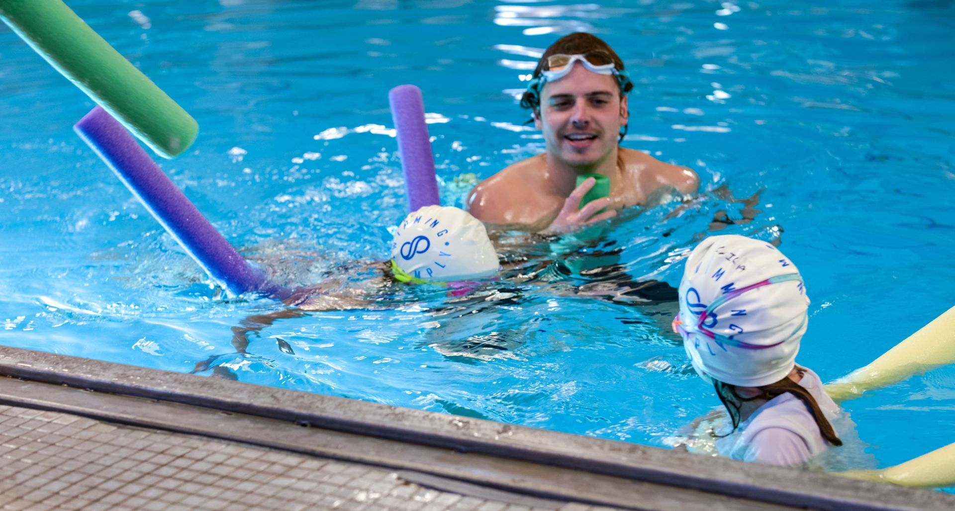 A man is teaching two children how to swim in a swimming pool.