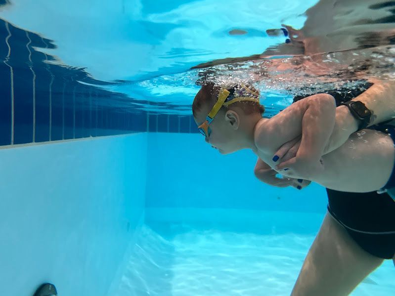 A woman is holding a baby underwater in a swimming pool.