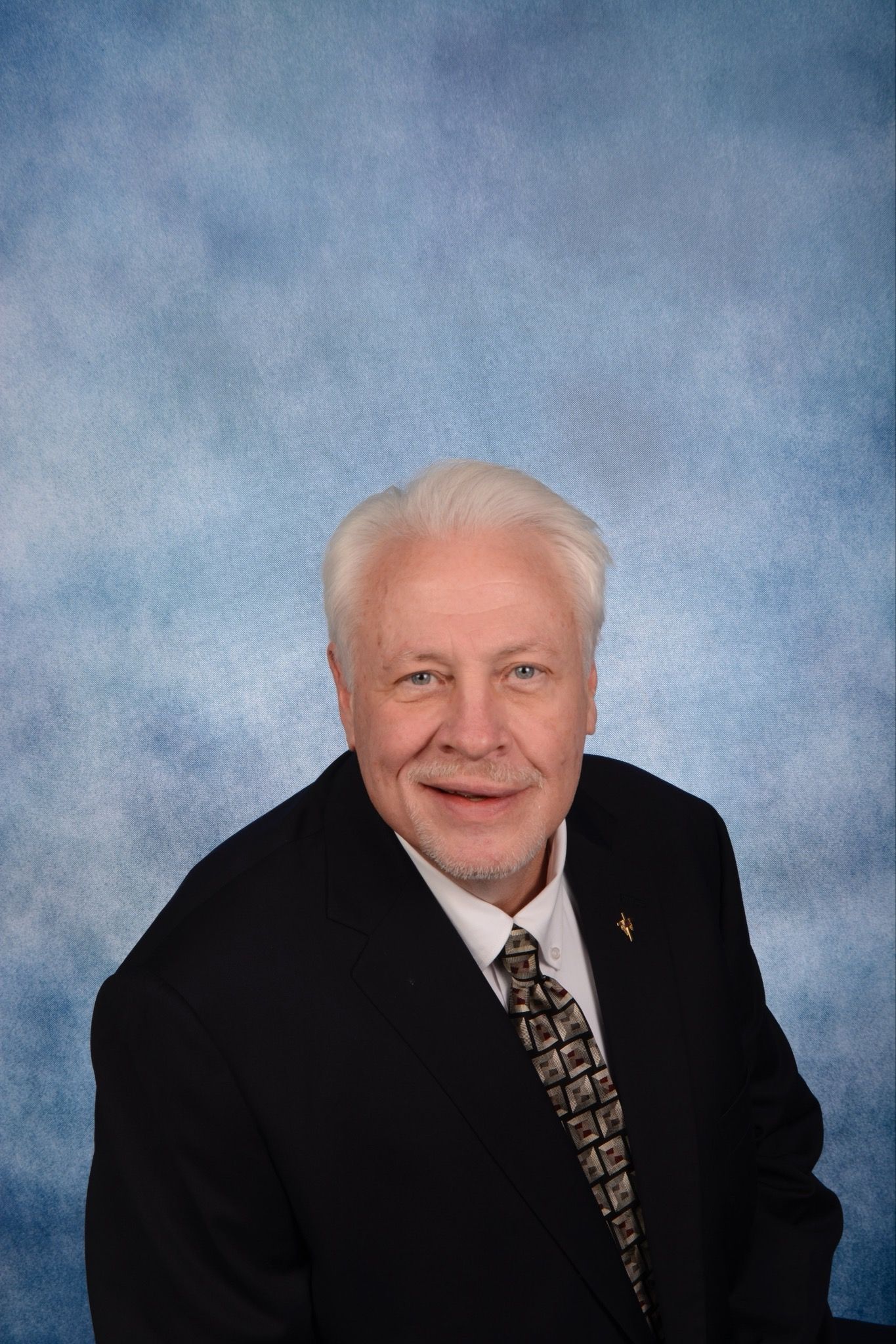 A man in a suit and tie is smiling in front of a blue background