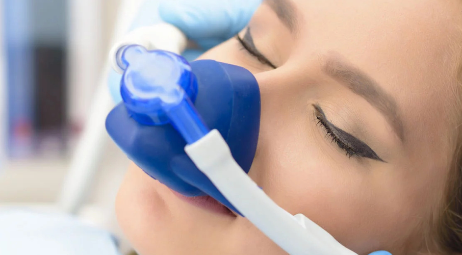 Woman with eyes closed, receiving dental sedation with a blue mask and white tubing.