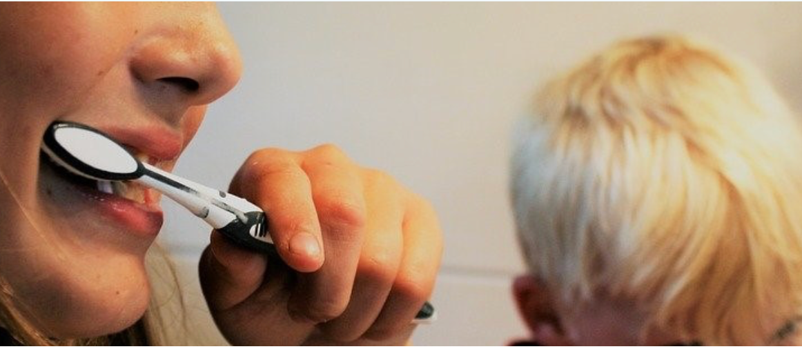 Person brushing teeth with another person nearby.