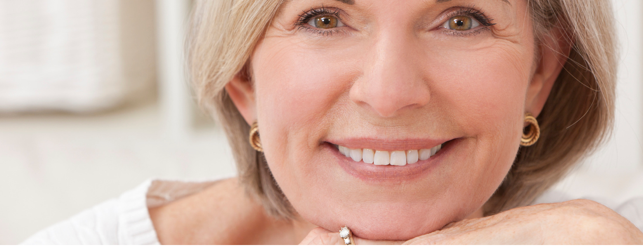 Woman smiling, resting chin on hands. Wearing gold earrings, light hair.