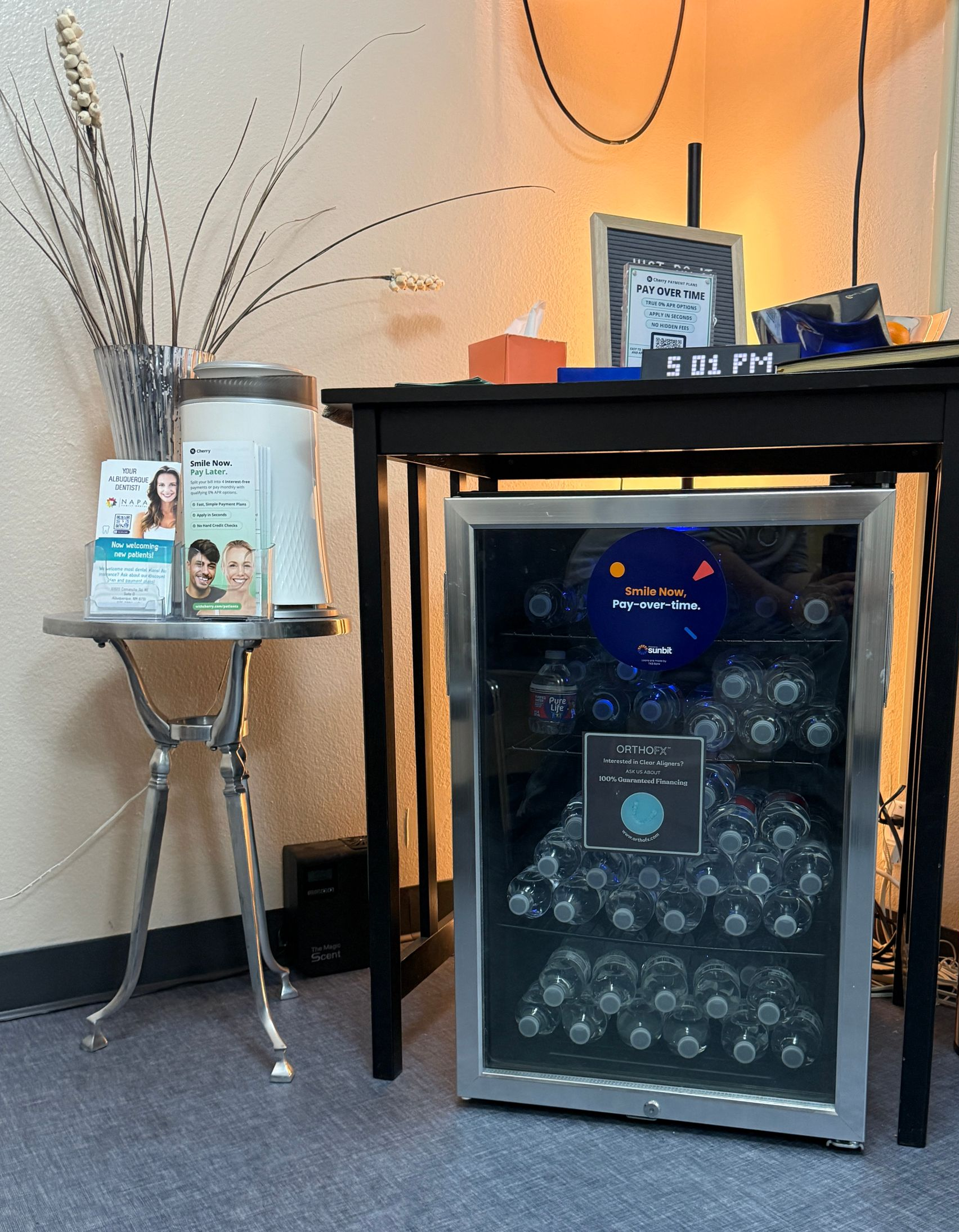 Water bottles in cooler beneath a black table, next to a small side table.