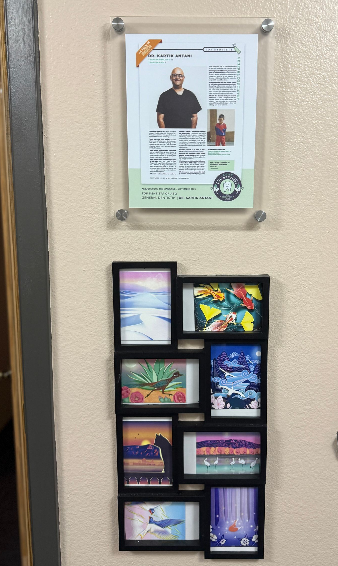 Wall with a framed ID card and a black multi-photo frame with colorful art prints.