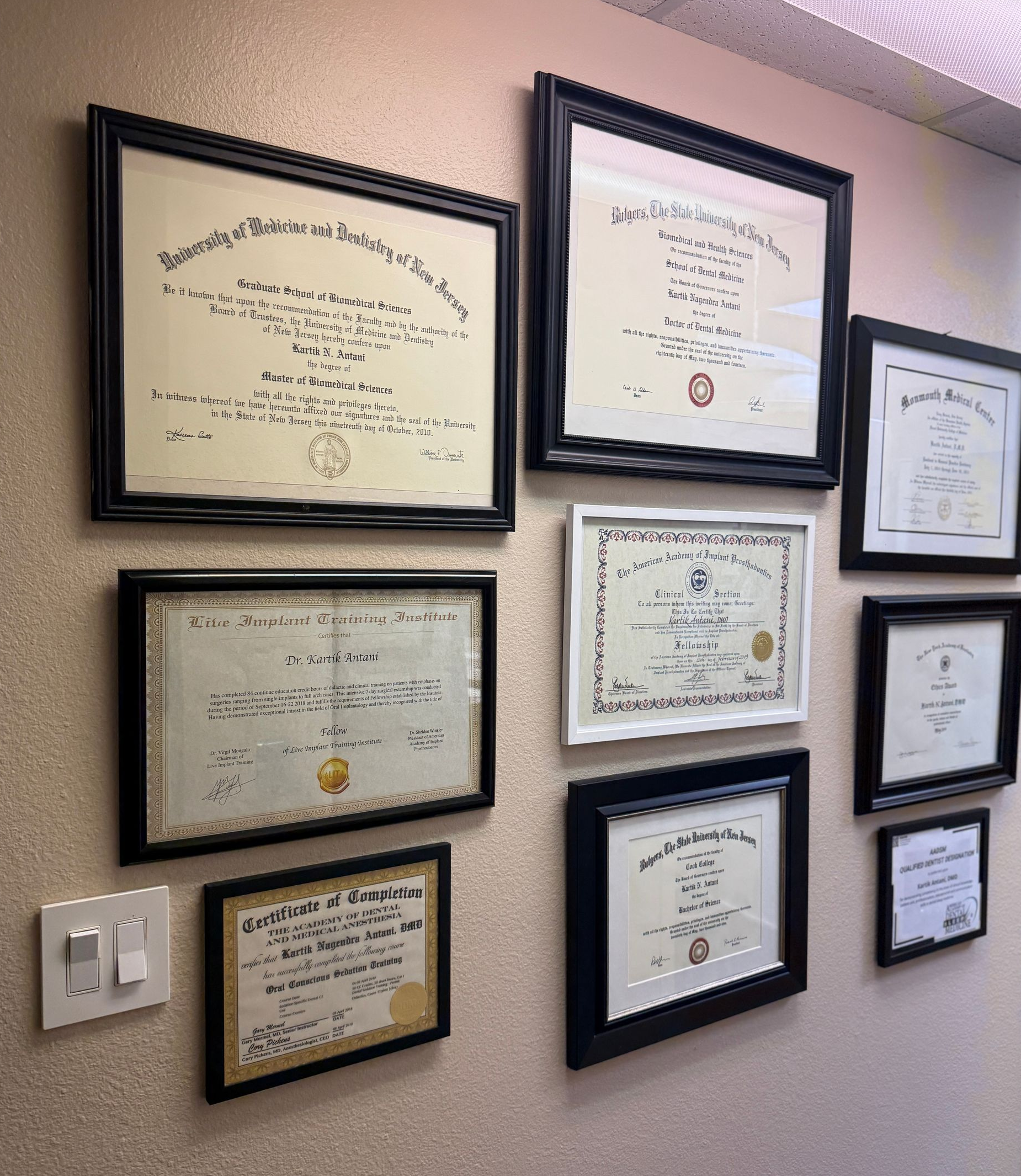 Wall with nine framed certificates, black frames, on a textured beige wall.