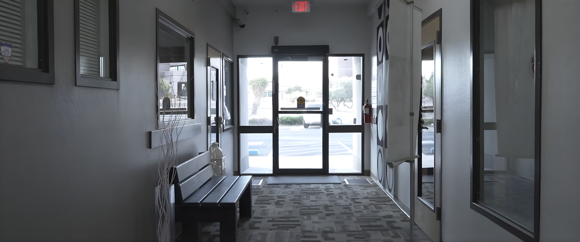 Hallway with a bench, windows, and an exit door. Gray walls and carpet.