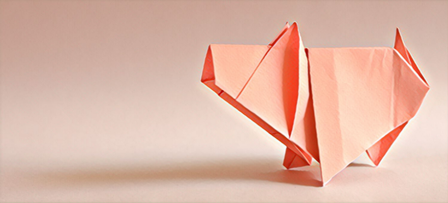 Un cochon en origami rose est assis sur une surface blanche.