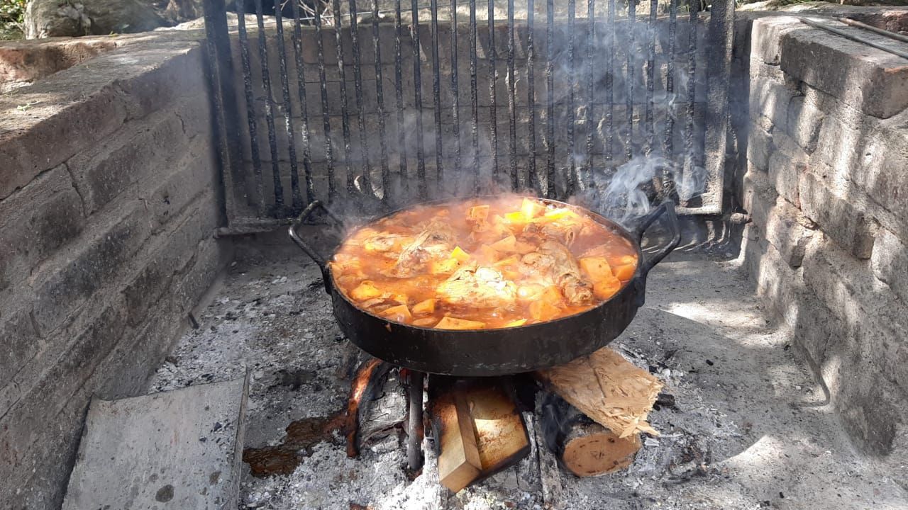 Guiso cocinándose en una olla grande sobre fuego de leña dentro de una estructura de ladrillo.