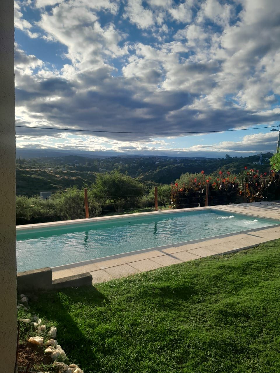 Una piscina rectangular domina un pintoresco valle verde bajo un cielo nublado.