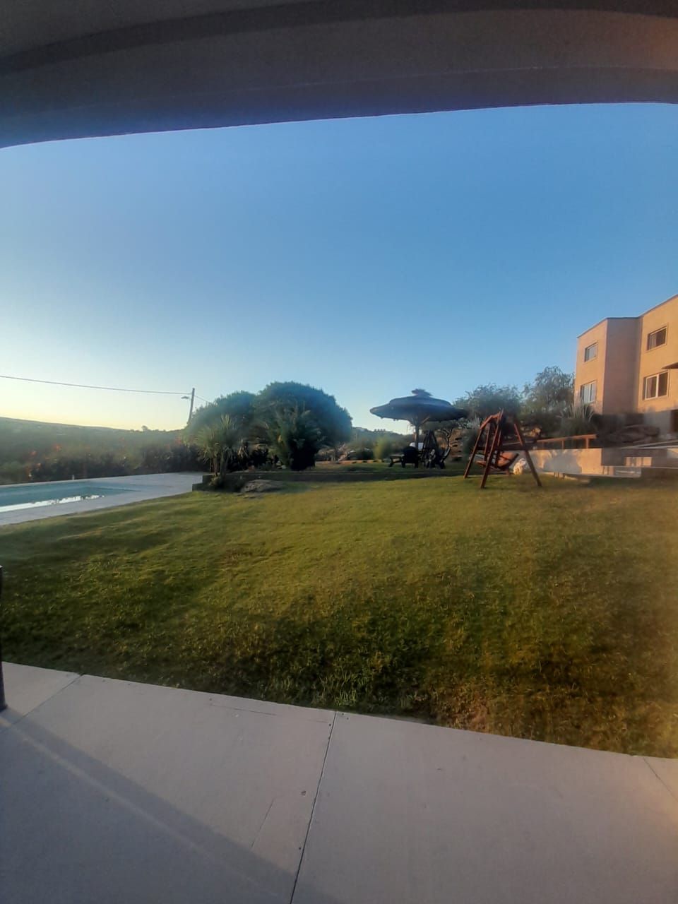 Césped verde, cielo azul, edificios y árboles en un entorno soleado al aire libre.