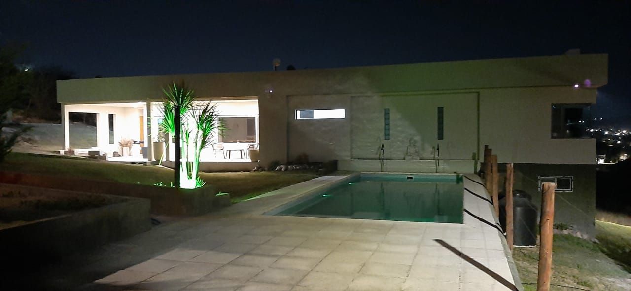 Una casa moderna de noche con piscina, luces y vista de la ciudad.