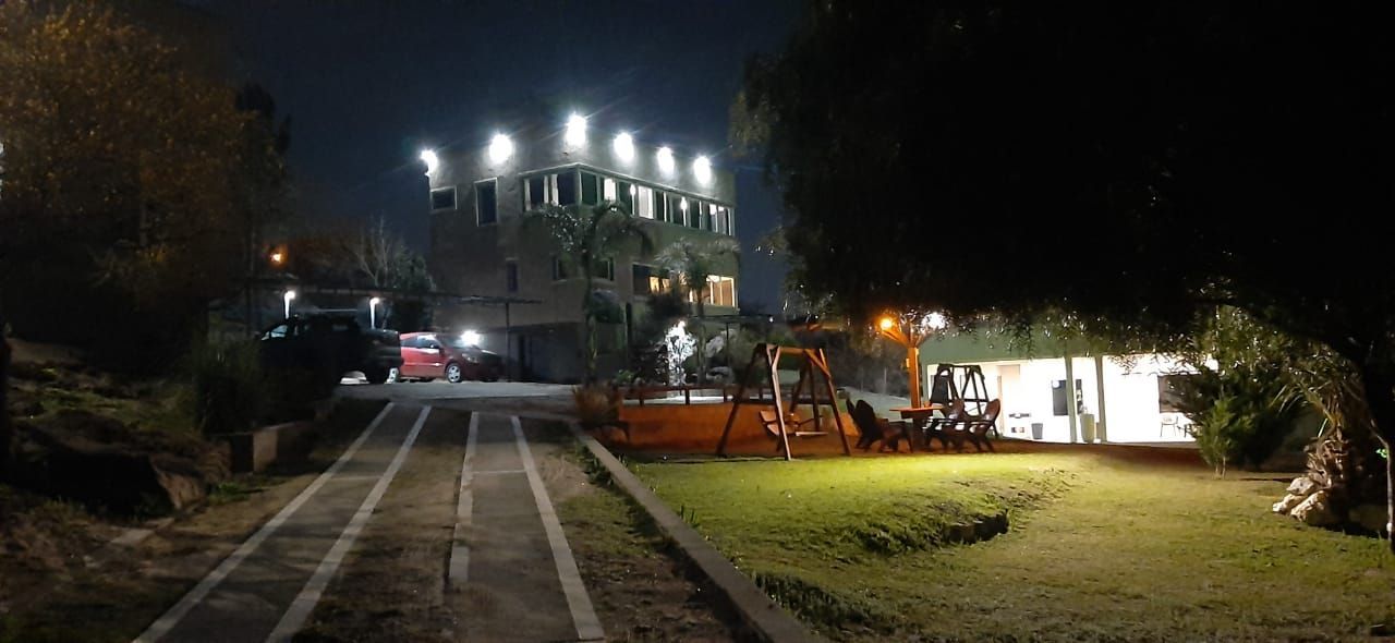 Vista nocturna de un edificio iluminado. Se ven un camión rojo y un parque infantil.