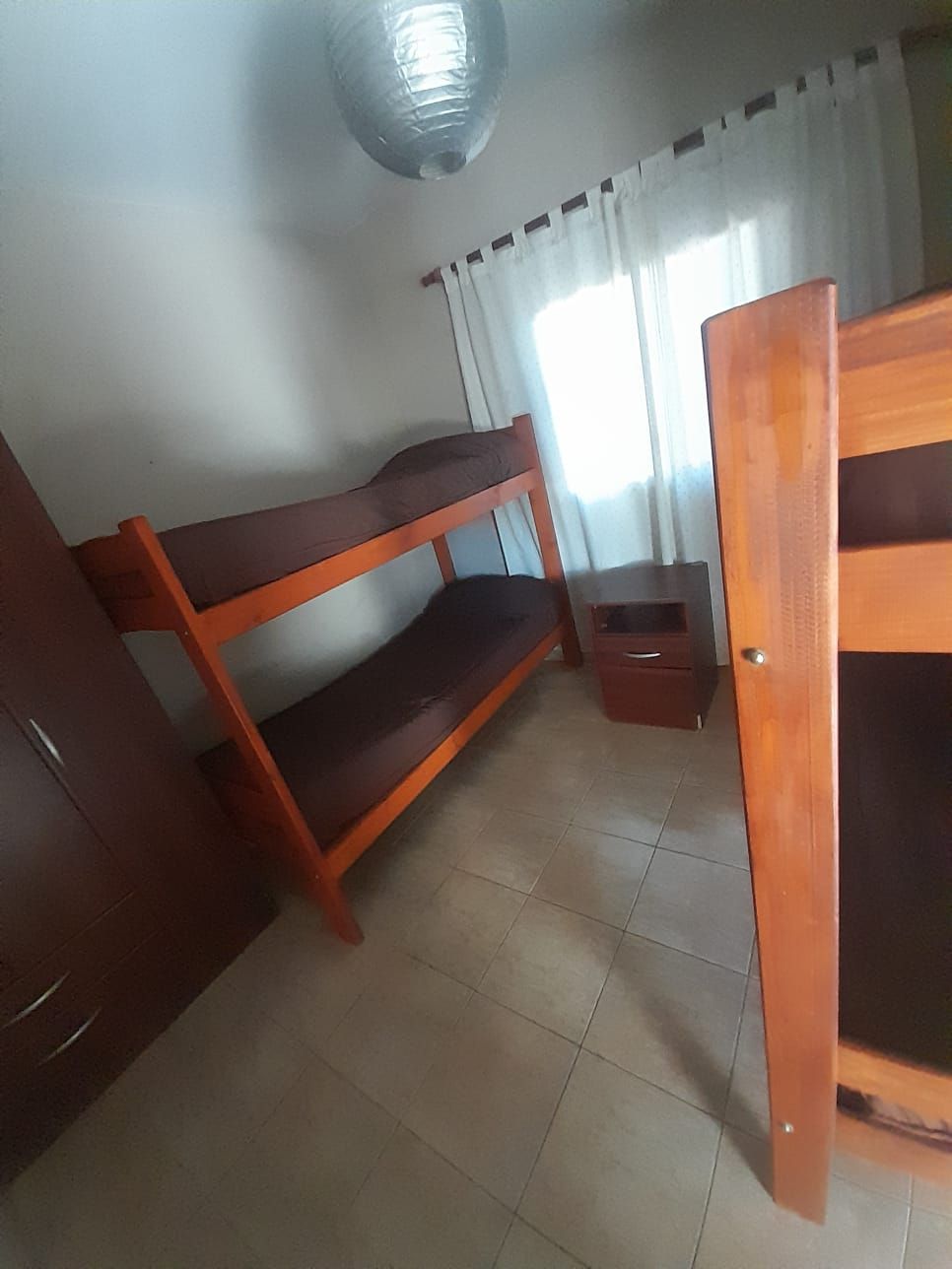 Baño con accesorios blancos, que incluyen inodoro, bidé y lavabo, piso oscuro, ducha y espejo.