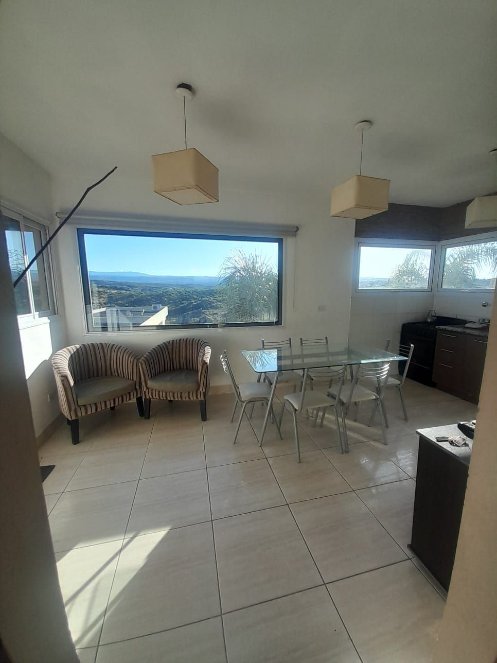 Baño pequeño con lavabo de pedestal, inodoro y espejo arqueado. Paredes beige y luz natural.