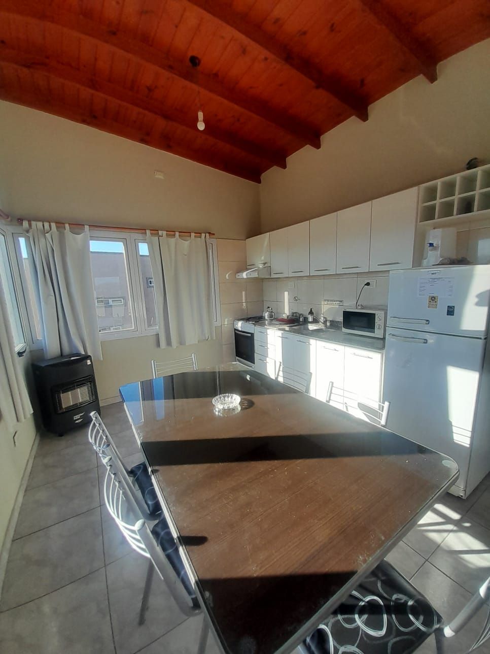 Cocina abierta y sala de estar con asiento junto a la ventana, mesa de comedor, electrodomésticos y TV montada.