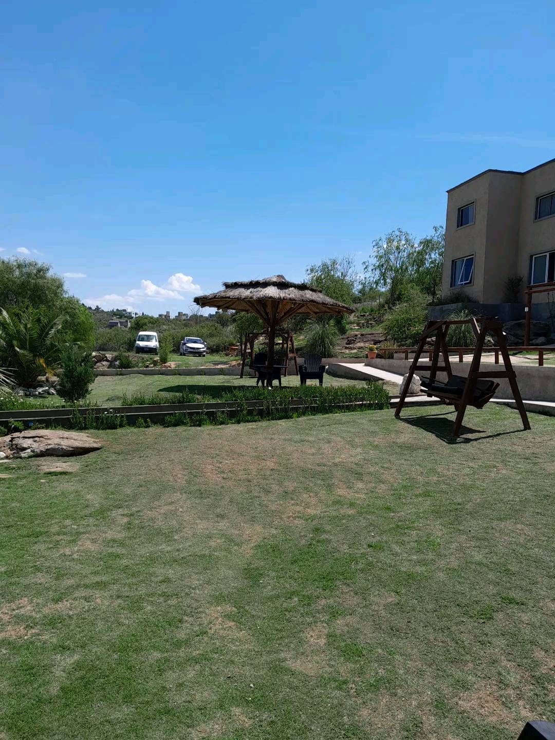 Césped con cenador, columpio y edificio en un día soleado.