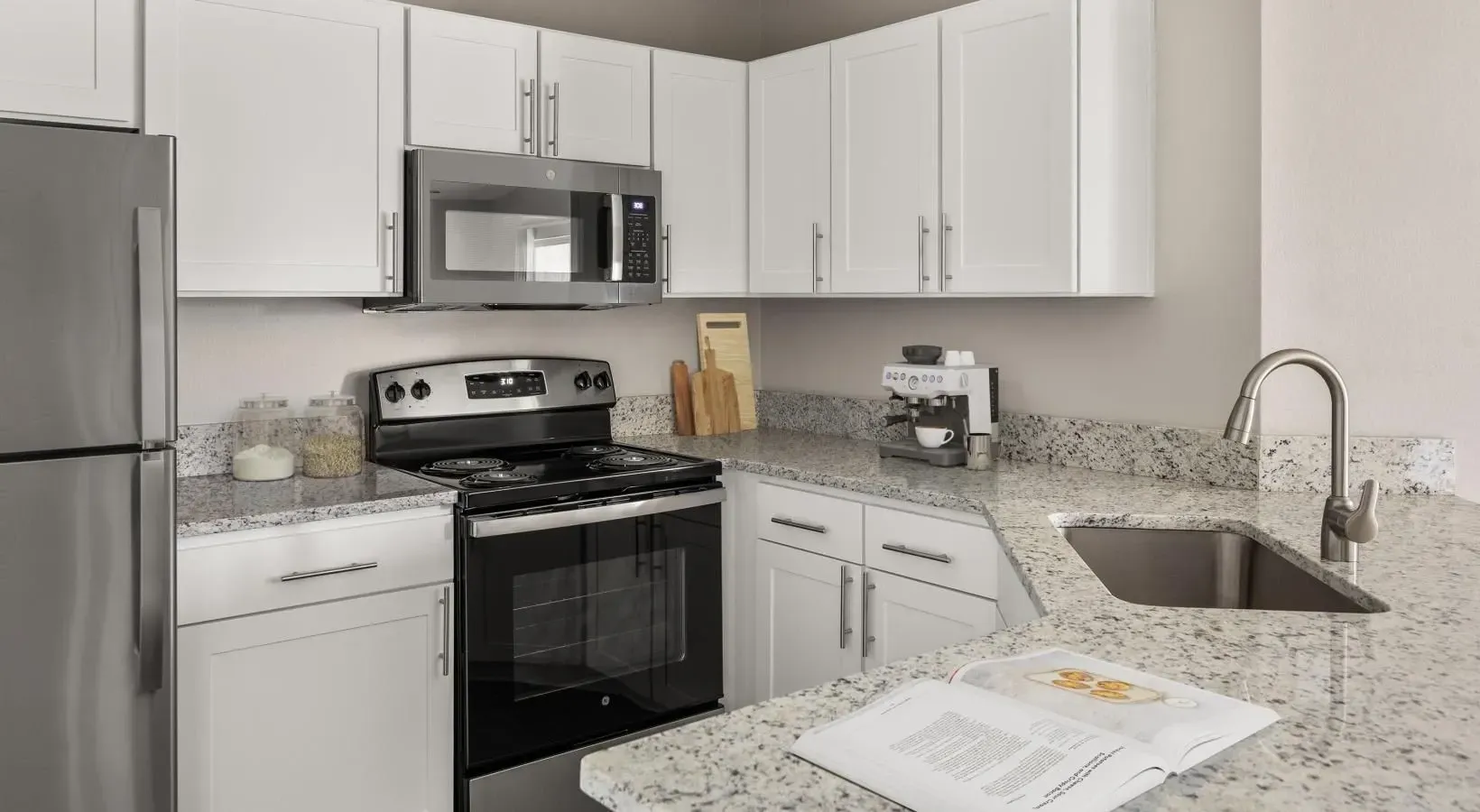 Modern kitchen with white cabinets, granite countertops, stainless steel appliances, and an open island.