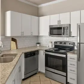 A modern kitchen with white cabinets, light speckled countertops, stainless steel appliances, and a subway tile backsplash.