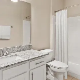 A bright, modern bathroom with a white vanity, granite countertop, neutral walls, and a shower with a white curtain.