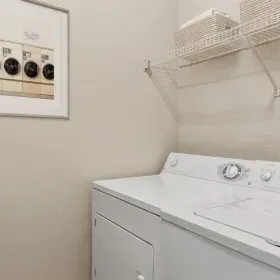 A laundry room featuring a white washer and dryer, a framed art print of laundry knobs, and a wire shelf above.