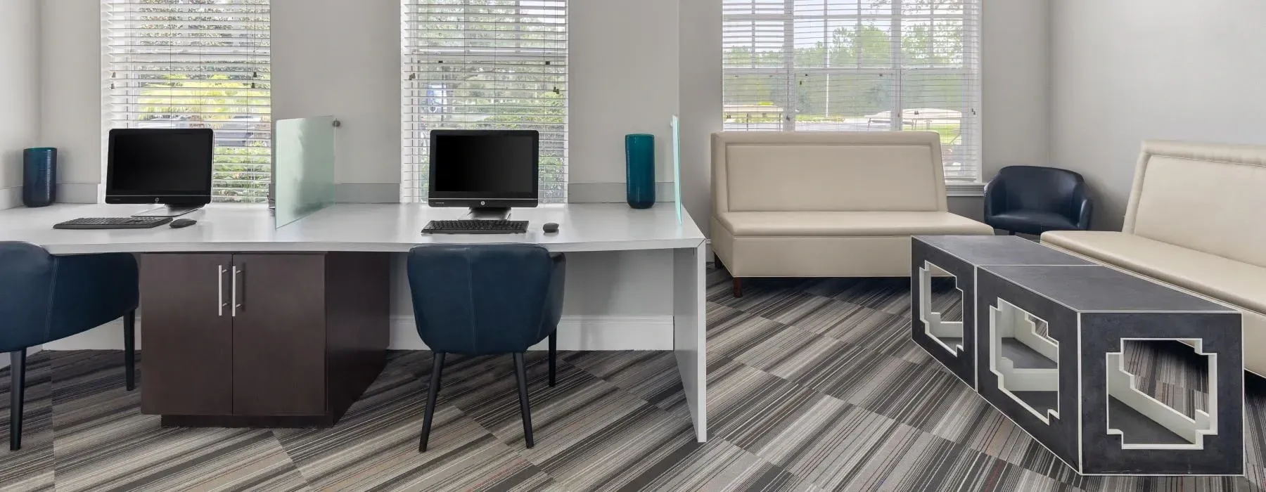 A shared office space featuring two computer workstations, a beige sofa, blue armchairs, and a patterned rug.