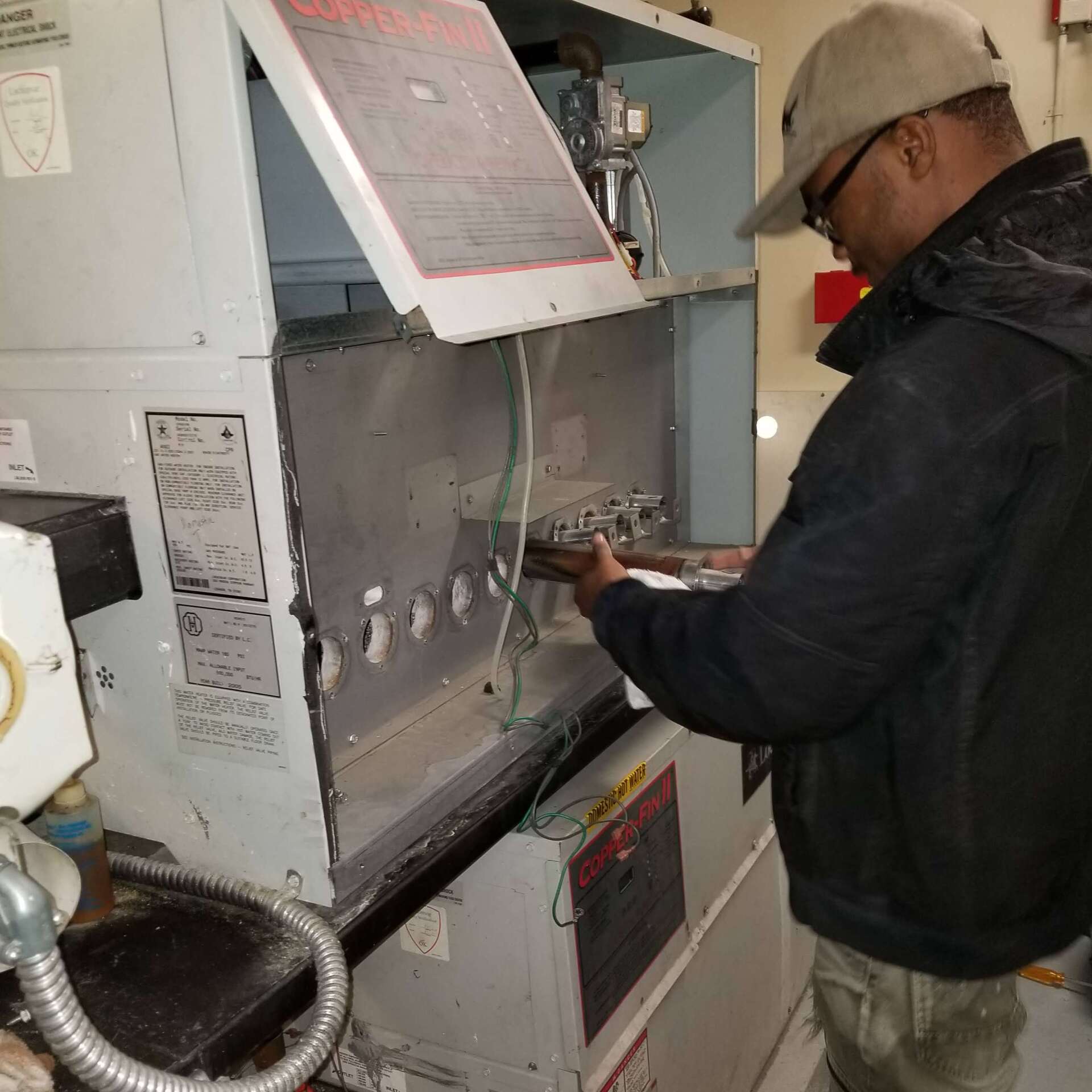 Man in cap working on a machine, likely repairing it. Indoors.