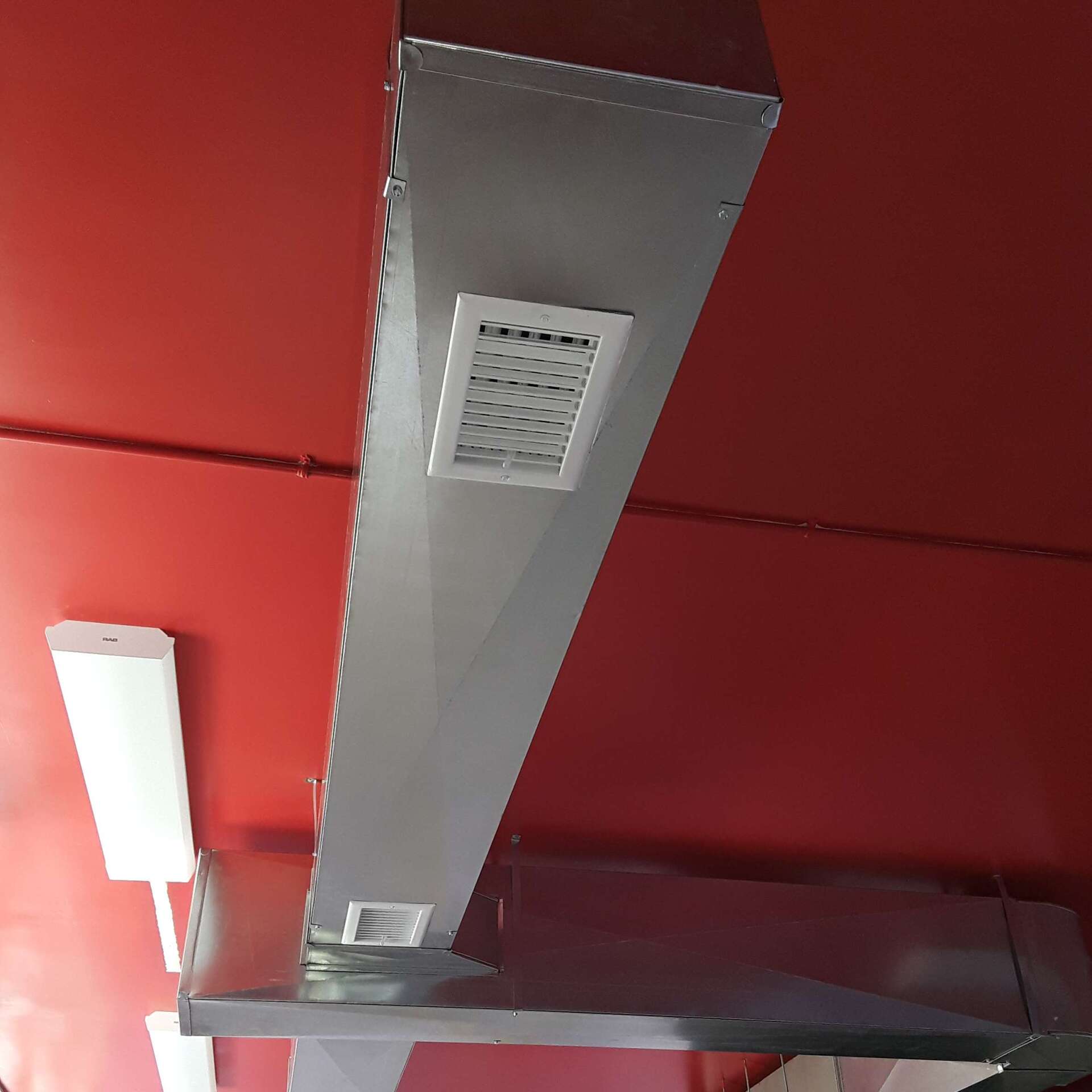 Metal HVAC ductwork on red ceiling, with vent.