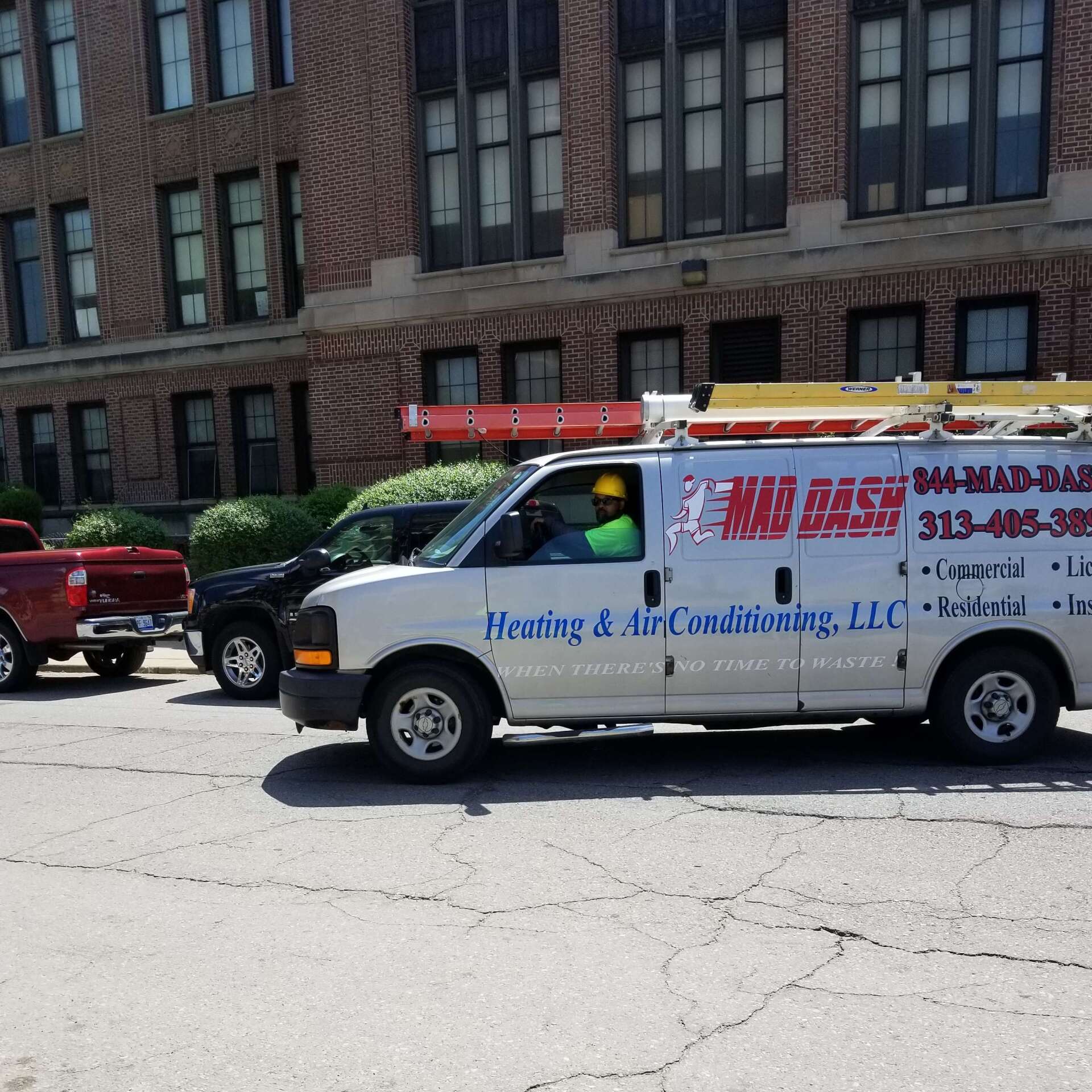 HVAC van with a ladder parked in front of a brick building, a person in the driver's seat.