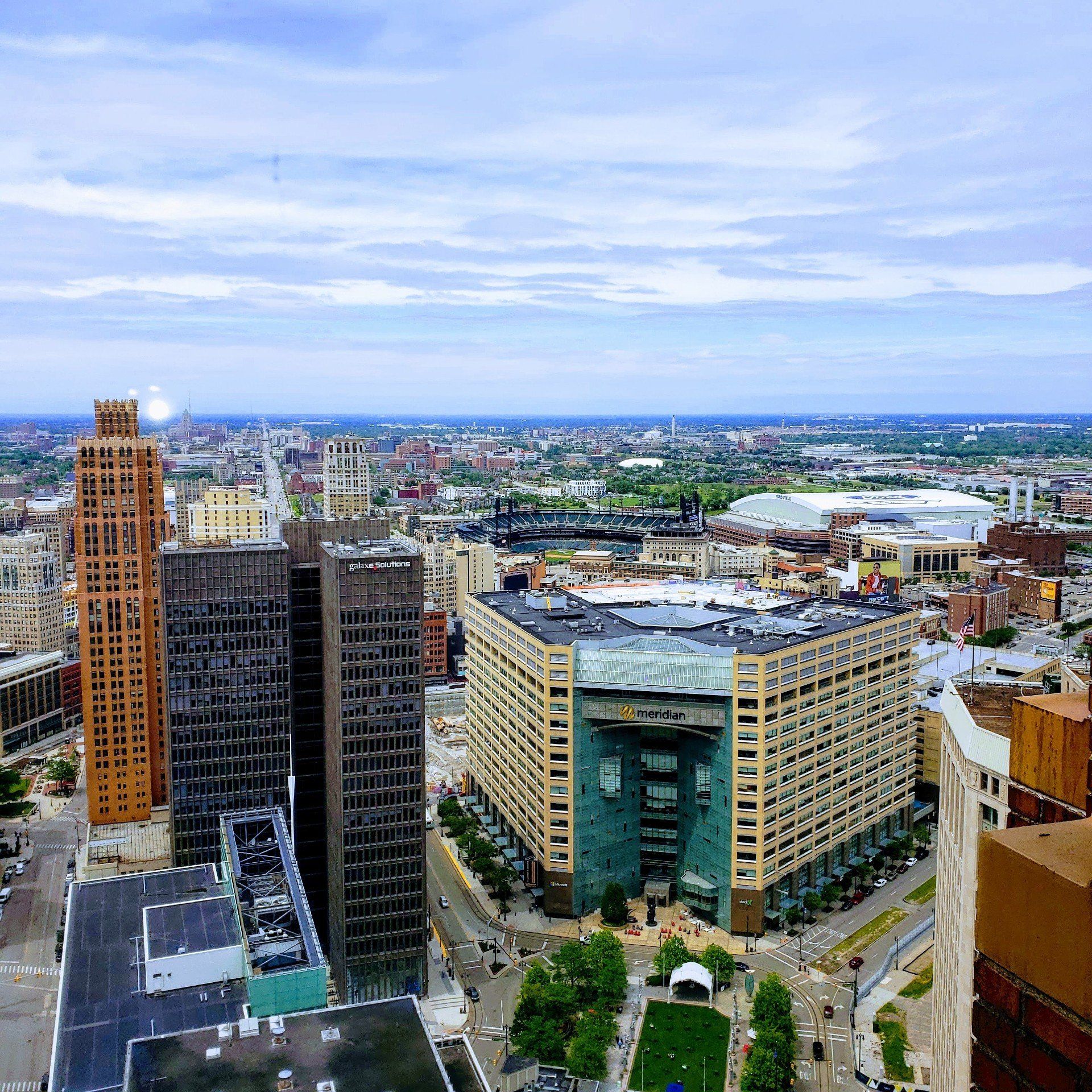 Cityscape of Detroit, Michigan: skyscrapers, buildings, stadium, green space, overcast sky.