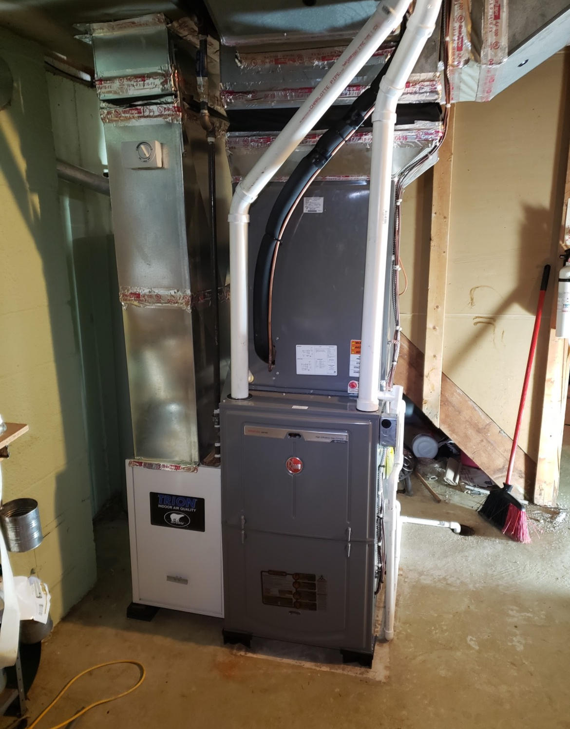 HVAC system with furnace and air handler in a basement setting. Silver ductwork, white pipes, gray unit.