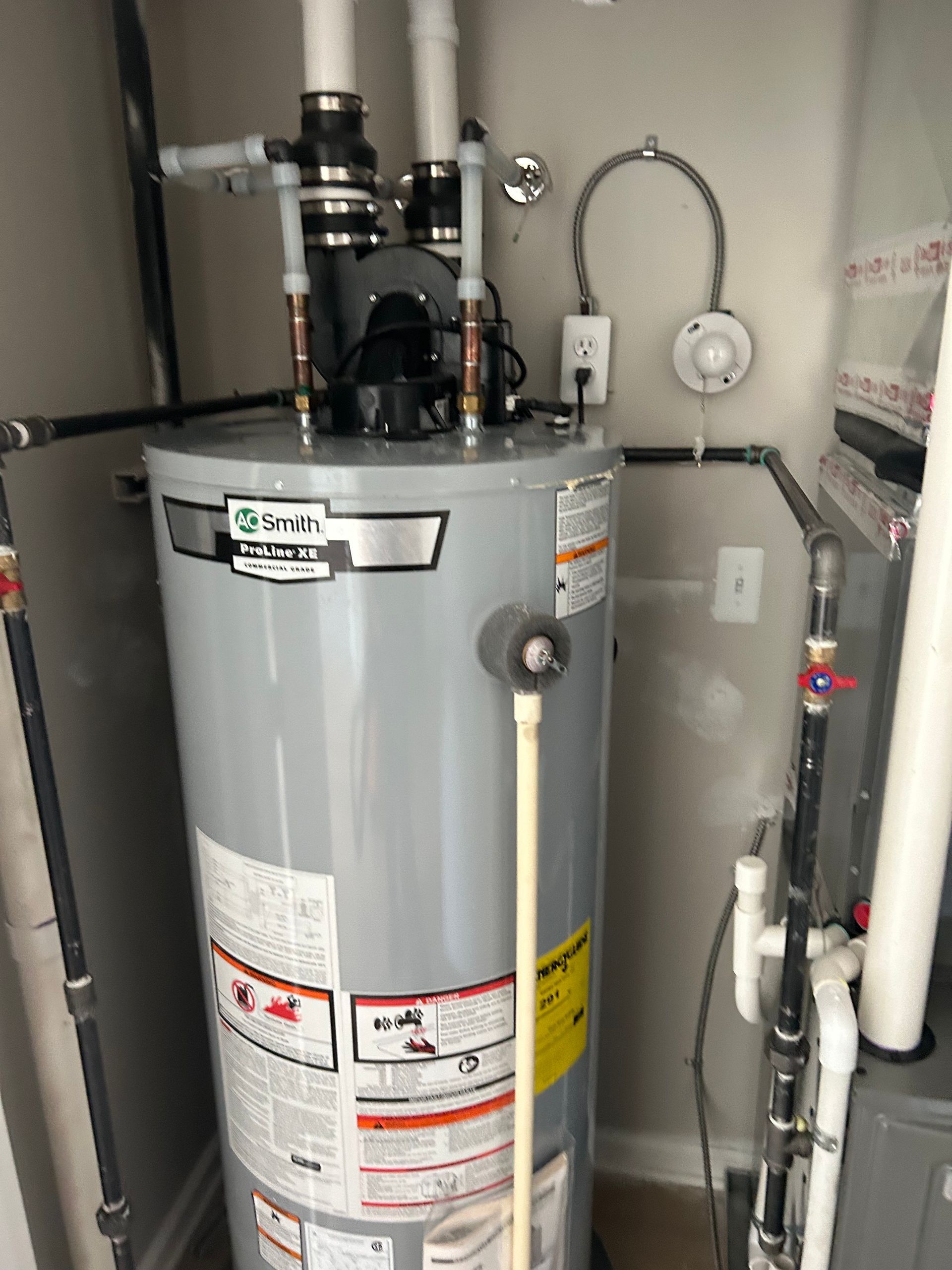 A gas water heater in a utility closet, with pipes and a smoke detector nearby.