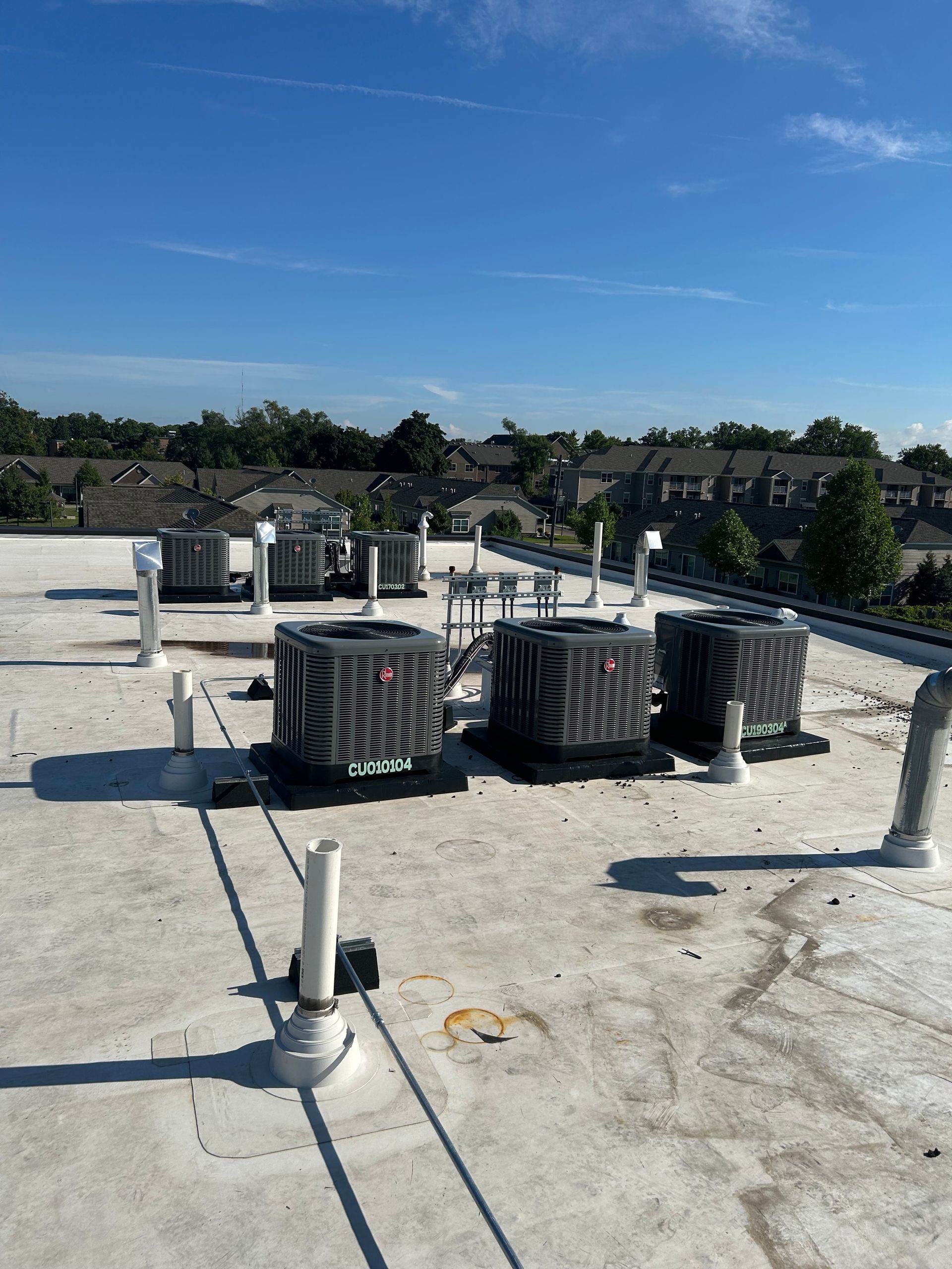 Rooftop with several air conditioning units and vents against a clear blue sky.