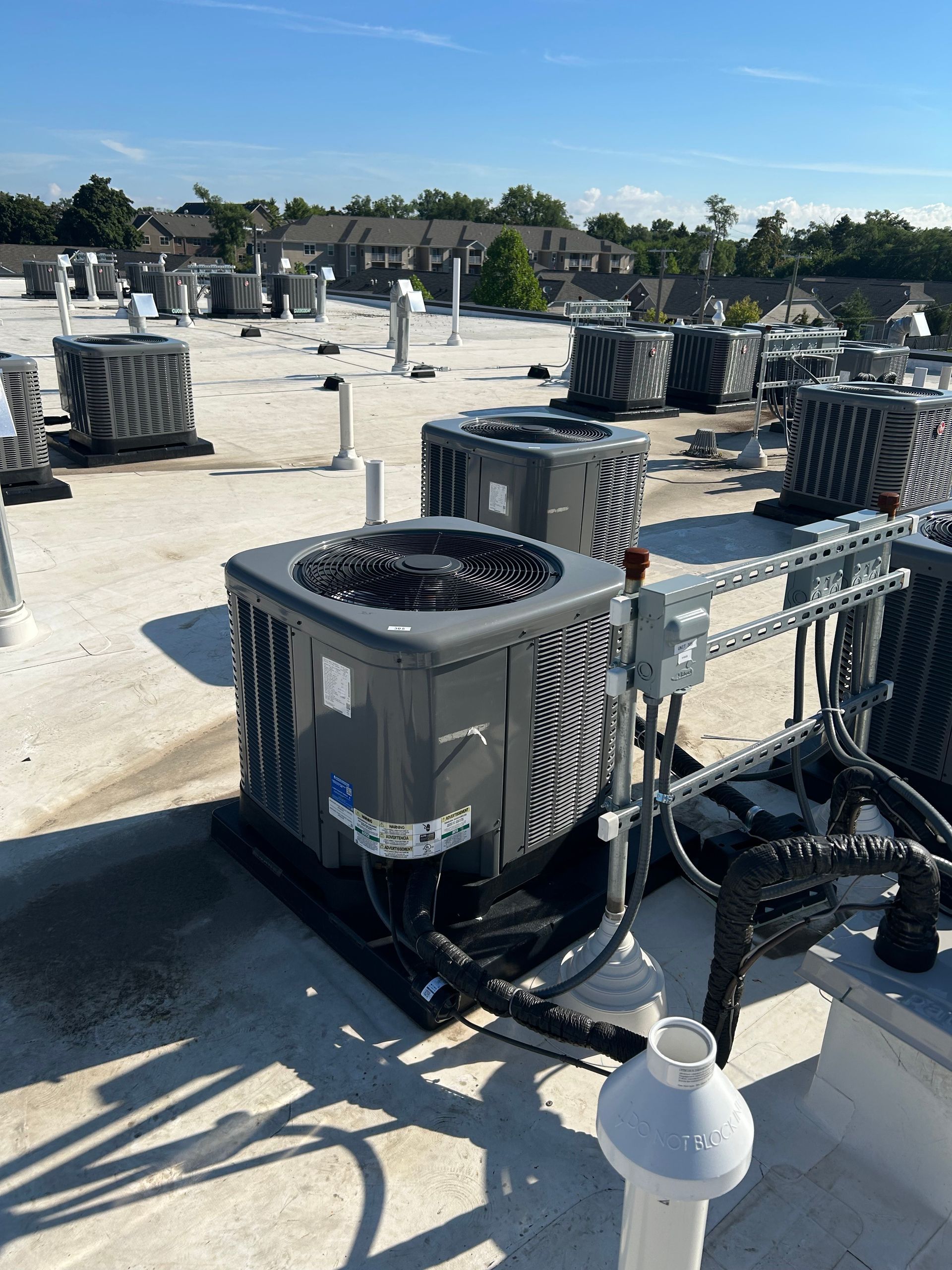 Air conditioning units on a white roof under a blue sky; several similar units are visible in the background.
