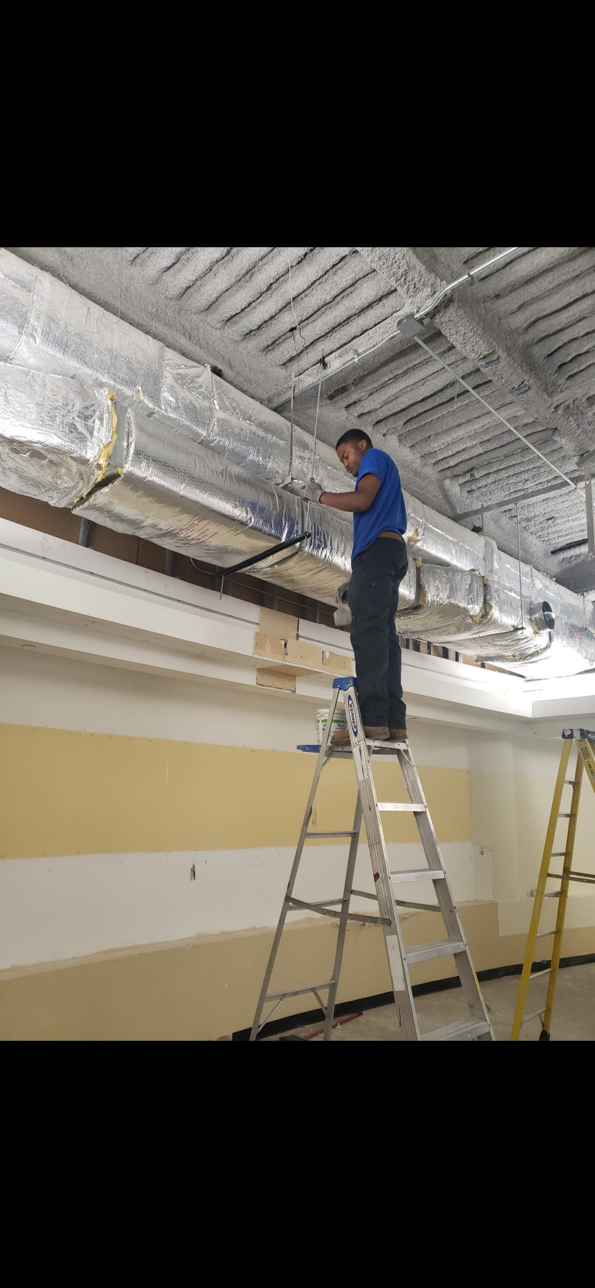 A person working on a duct system while standing on a ladder in a room.
