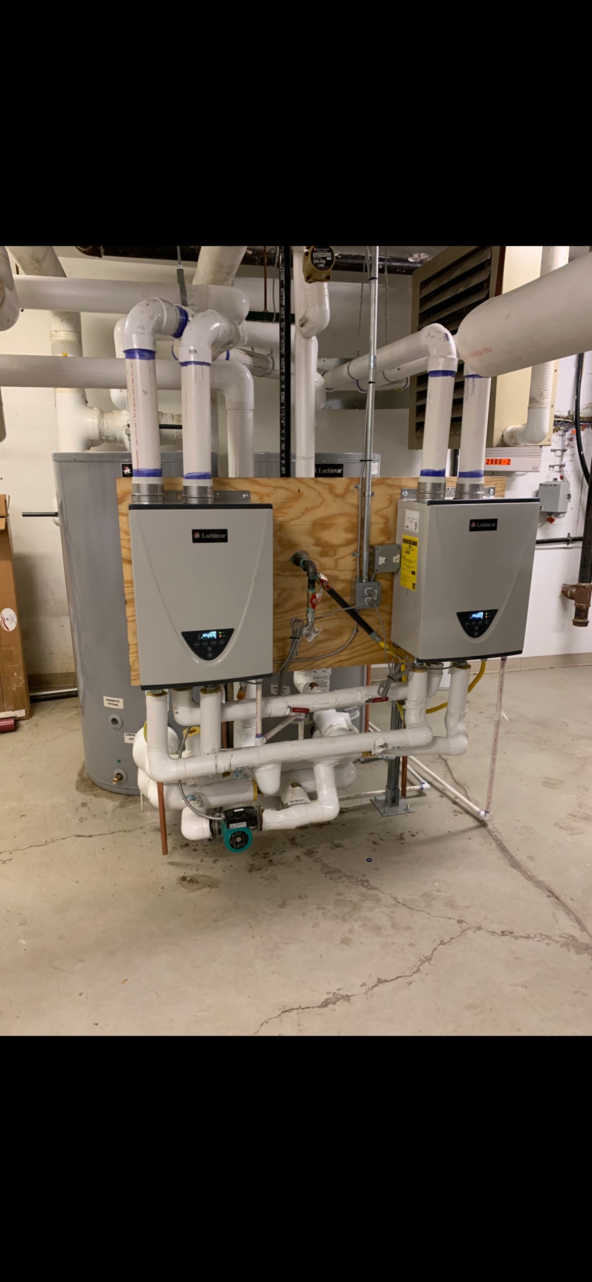 Two wall-mounted water heaters with connected piping in an industrial setting.