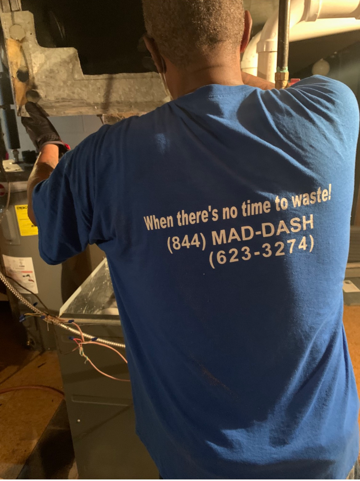 Person in blue shirt working on HVAC unit; company logo 