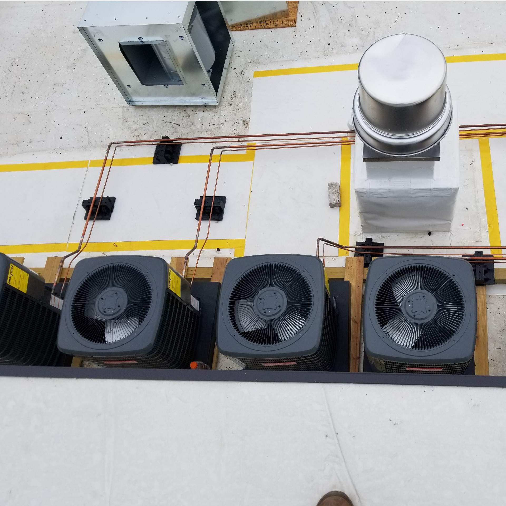 Rooftop HVAC units with copper pipes and a vent, on a white surface with yellow trim.