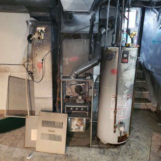 Furnace and water heater in a utility room. Grey metal appliances with detached panels.