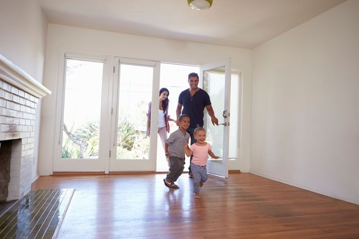A family is walking through an empty living room in their new home .