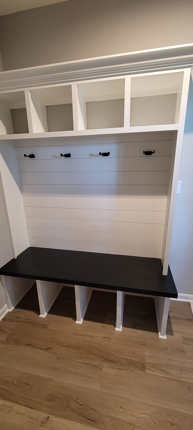 A mud room with a black bench and white shelves .