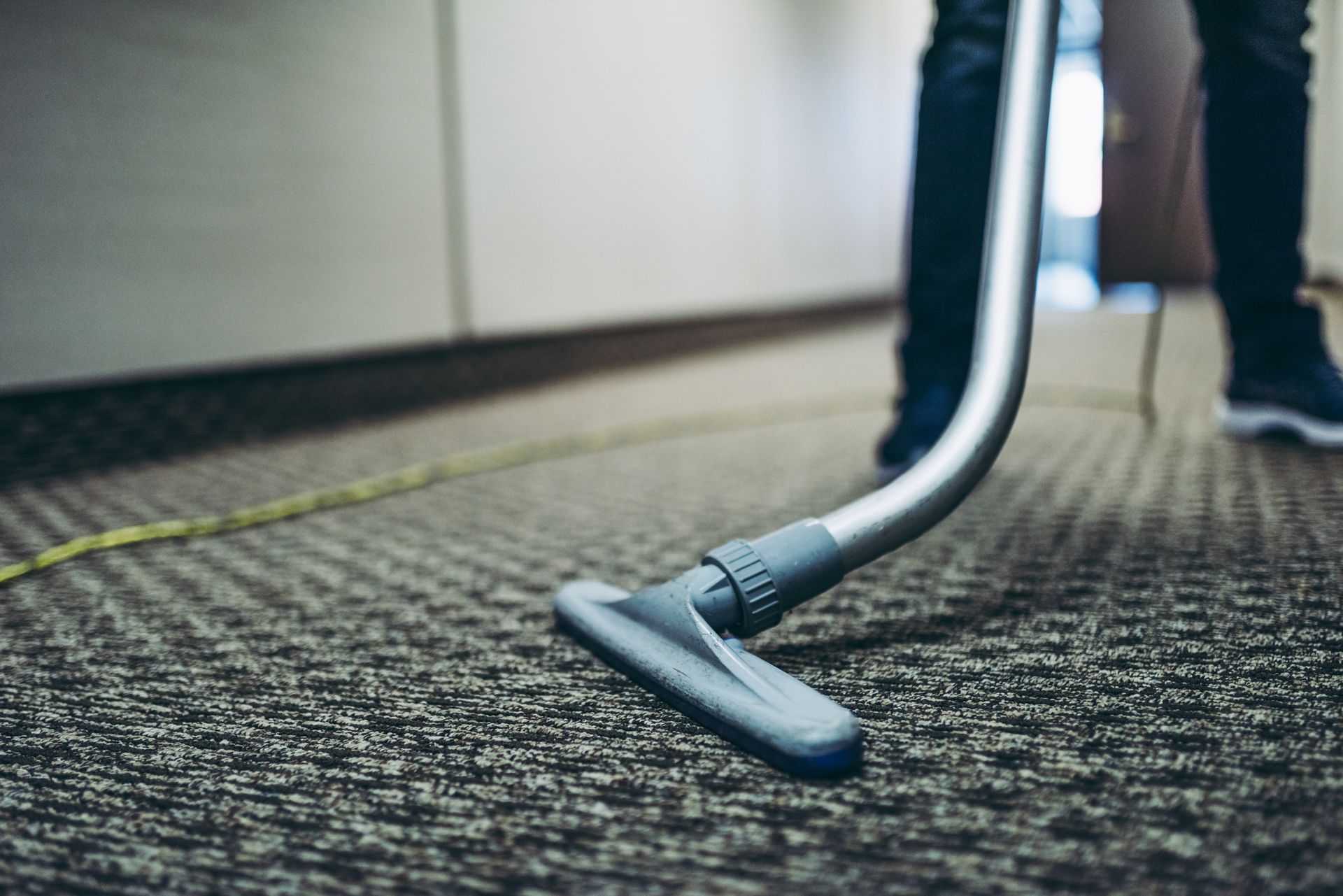 A janitor vacuums the carpet in the corridor of an office building.