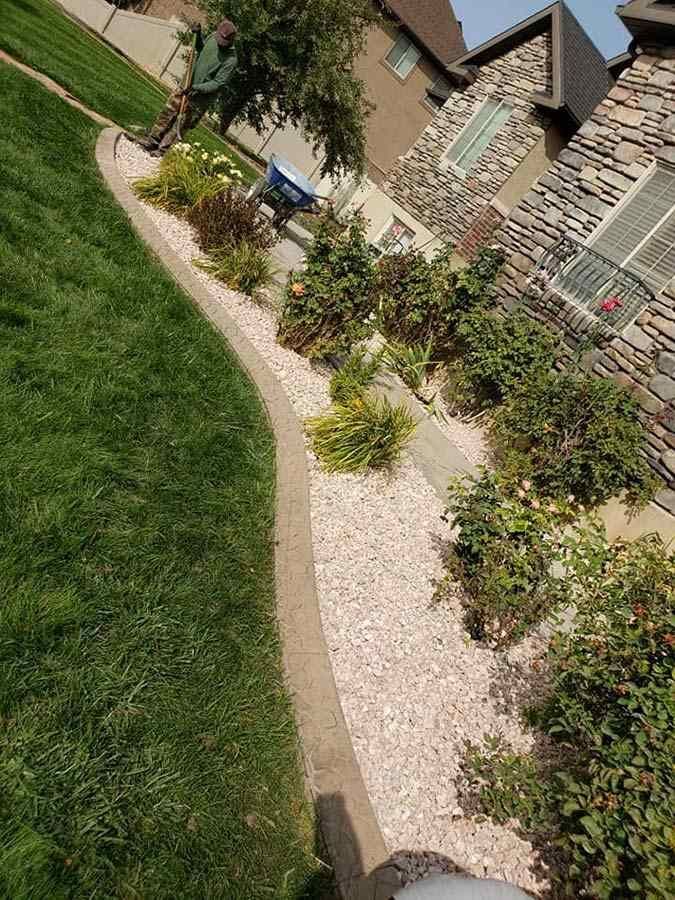 A man is standing next to a lush green lawn in front of a house.