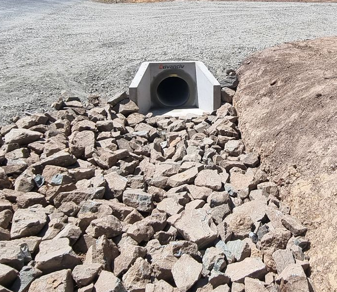 Concrete culvert entrance with large rocks for erosion control.