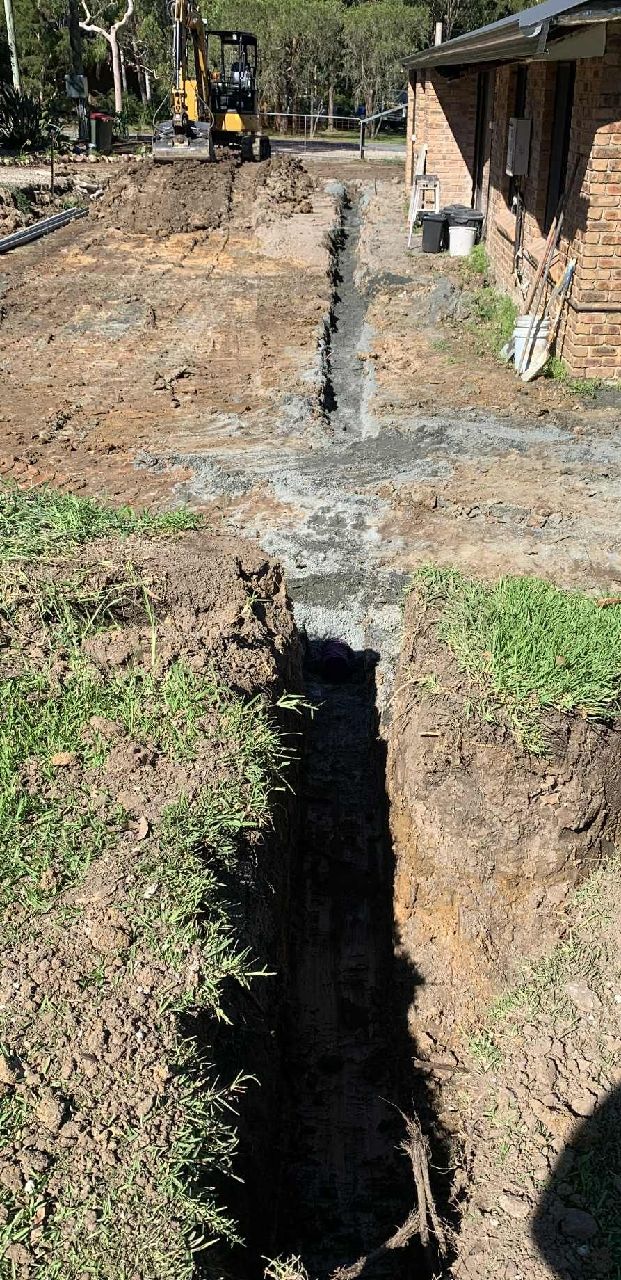 A deep trench dug in the ground near a house, construction site.