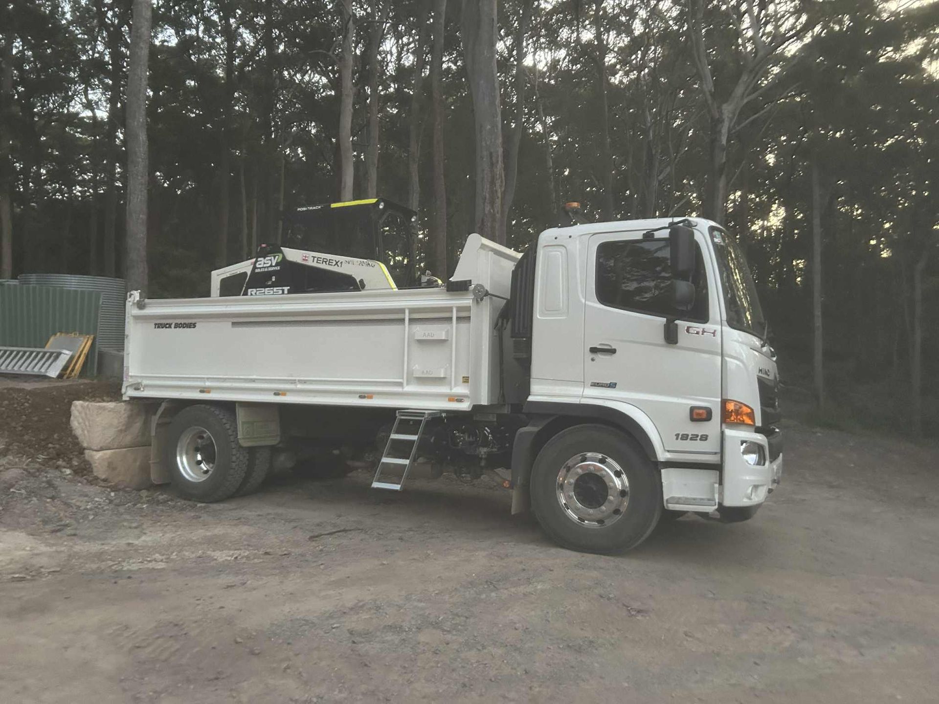 White dump truck parked on gravel in a wooded area.