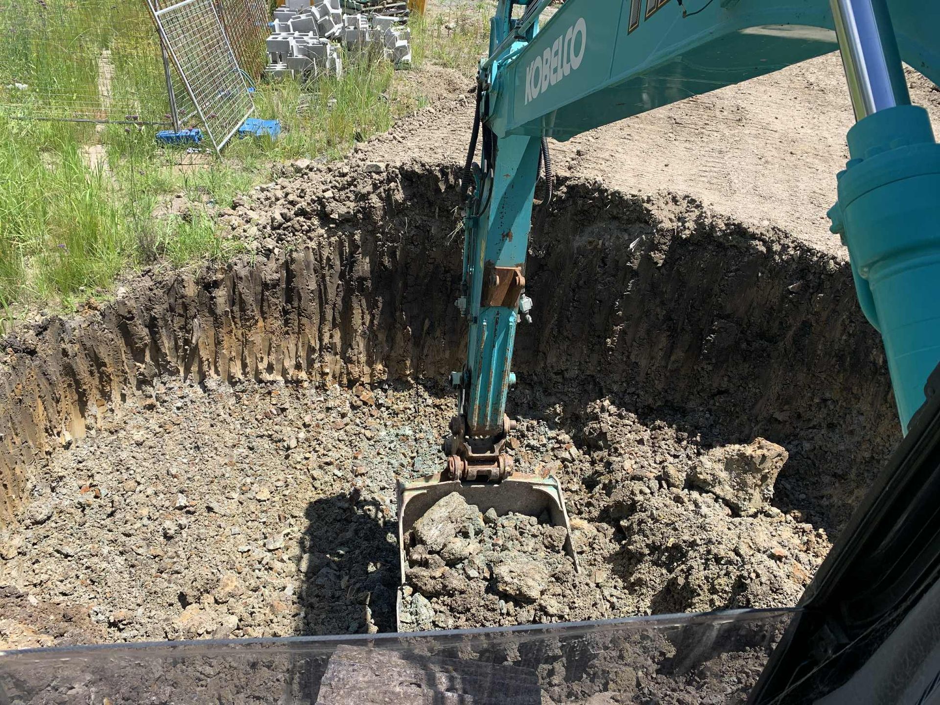 A teal excavator digs into a brown dirt bank, filling its scoop.