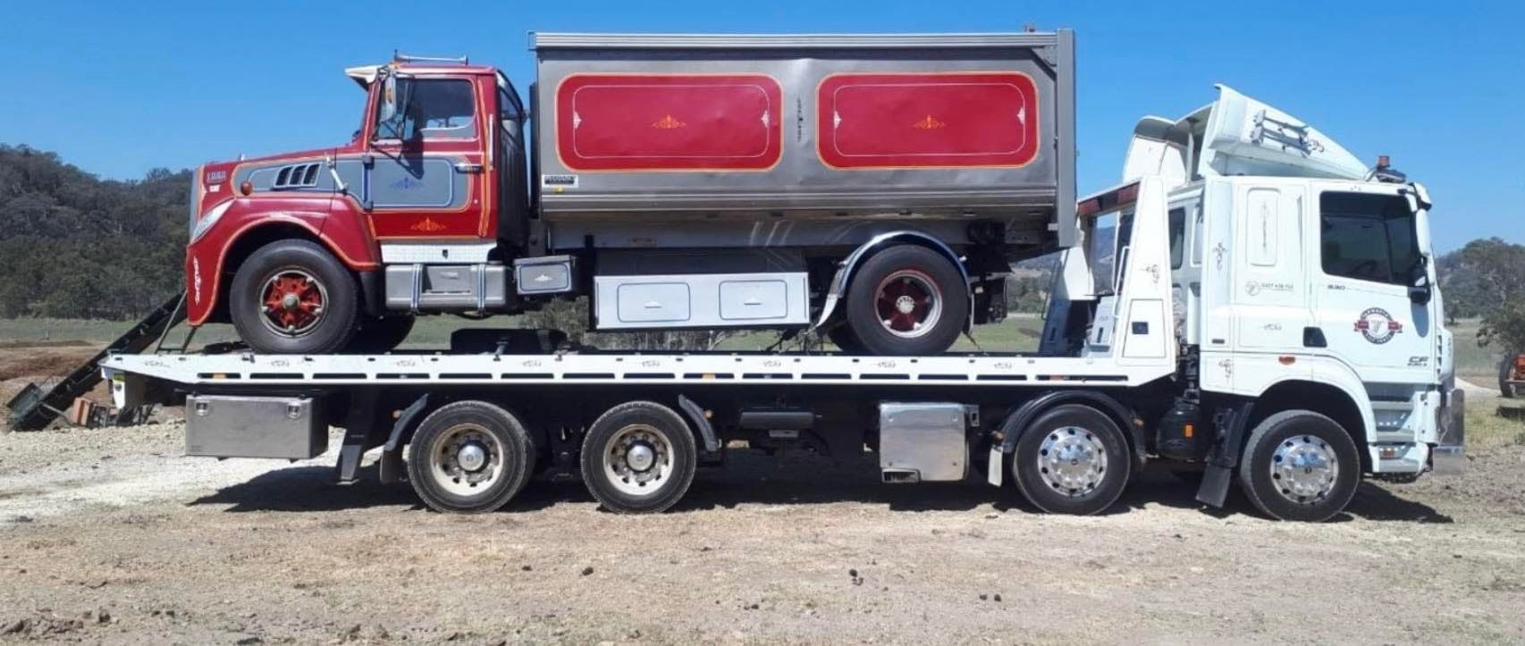 A Red Dump Truck Loaded on a White Flatbed Truck on a Sunny Day